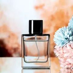 Elegancka butelka perfum z czarną nakrętką, obok bukiet pastelowych kwiatów. Chcesz wiedzieć, jak sprawdzić, czy perfumy są oryginalne?