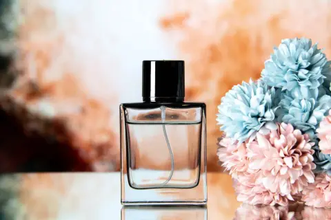 Elegancka butelka perfum z czarną nakrętką, obok bukiet pastelowych kwiatów. Chcesz wiedzieć, jak sprawdzić, czy perfumy są oryginalne?